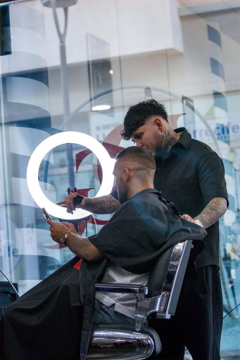 Barbero perfila a un cliente con capa de la UFC delante del espejo
