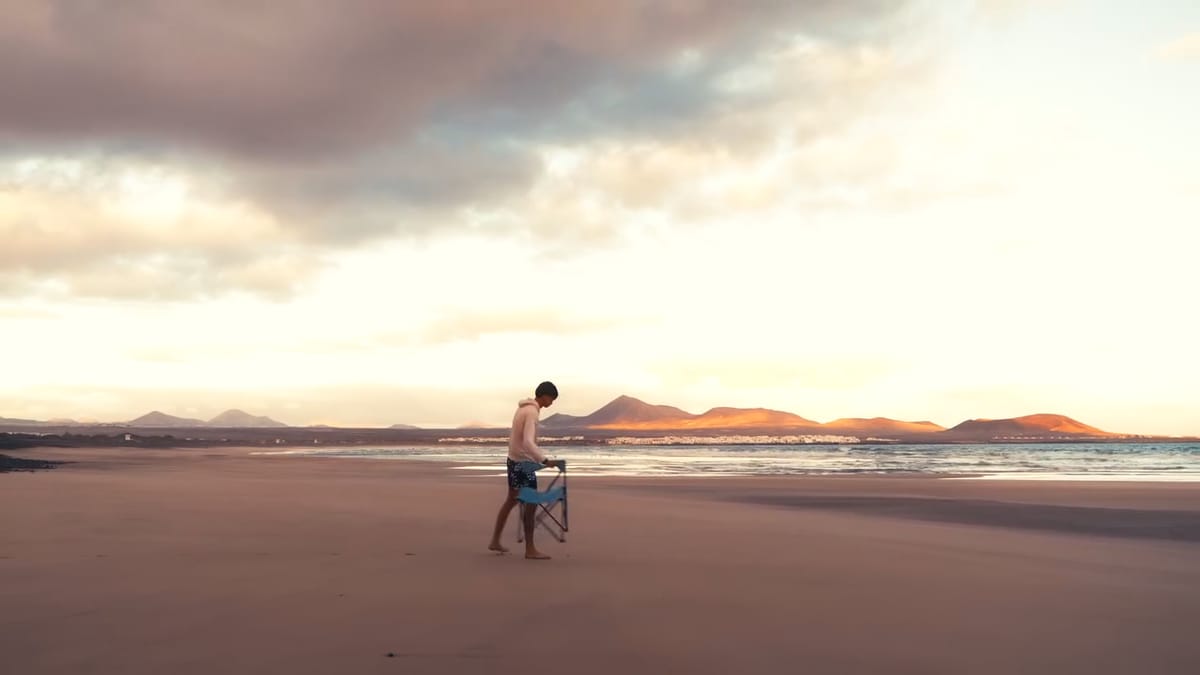Persona camina por la orilla de Famara con una silla plegable al atardecer