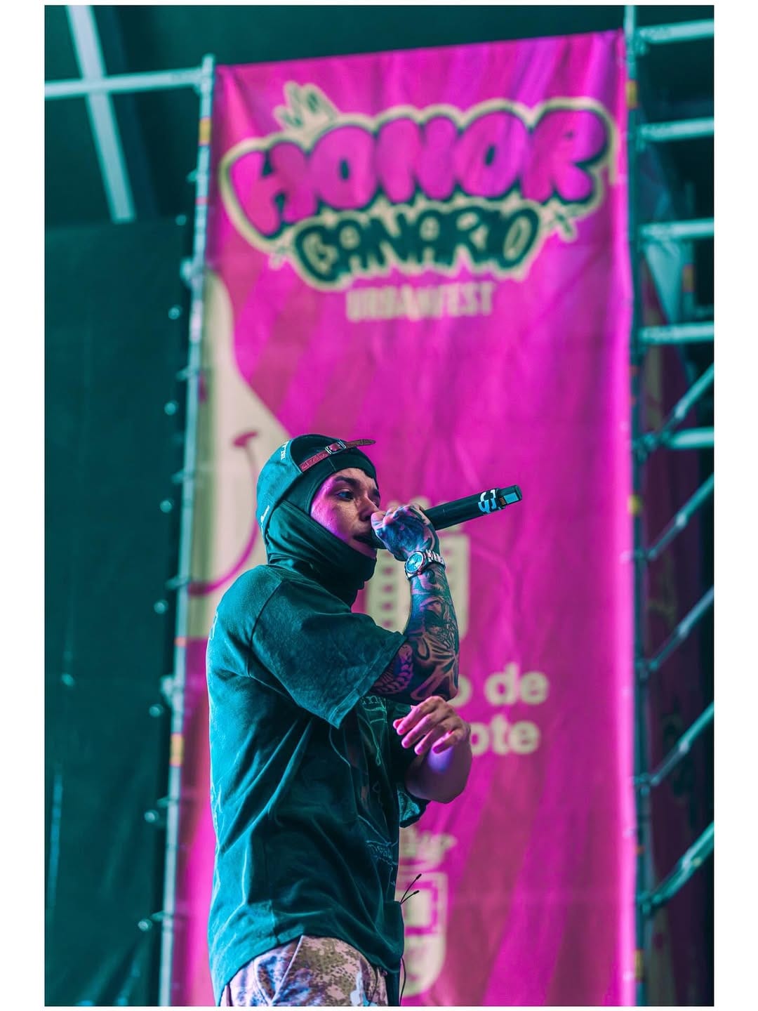 Artista con pasamontañas frente a la pancarta rosa del Honor Canario Urban Fest