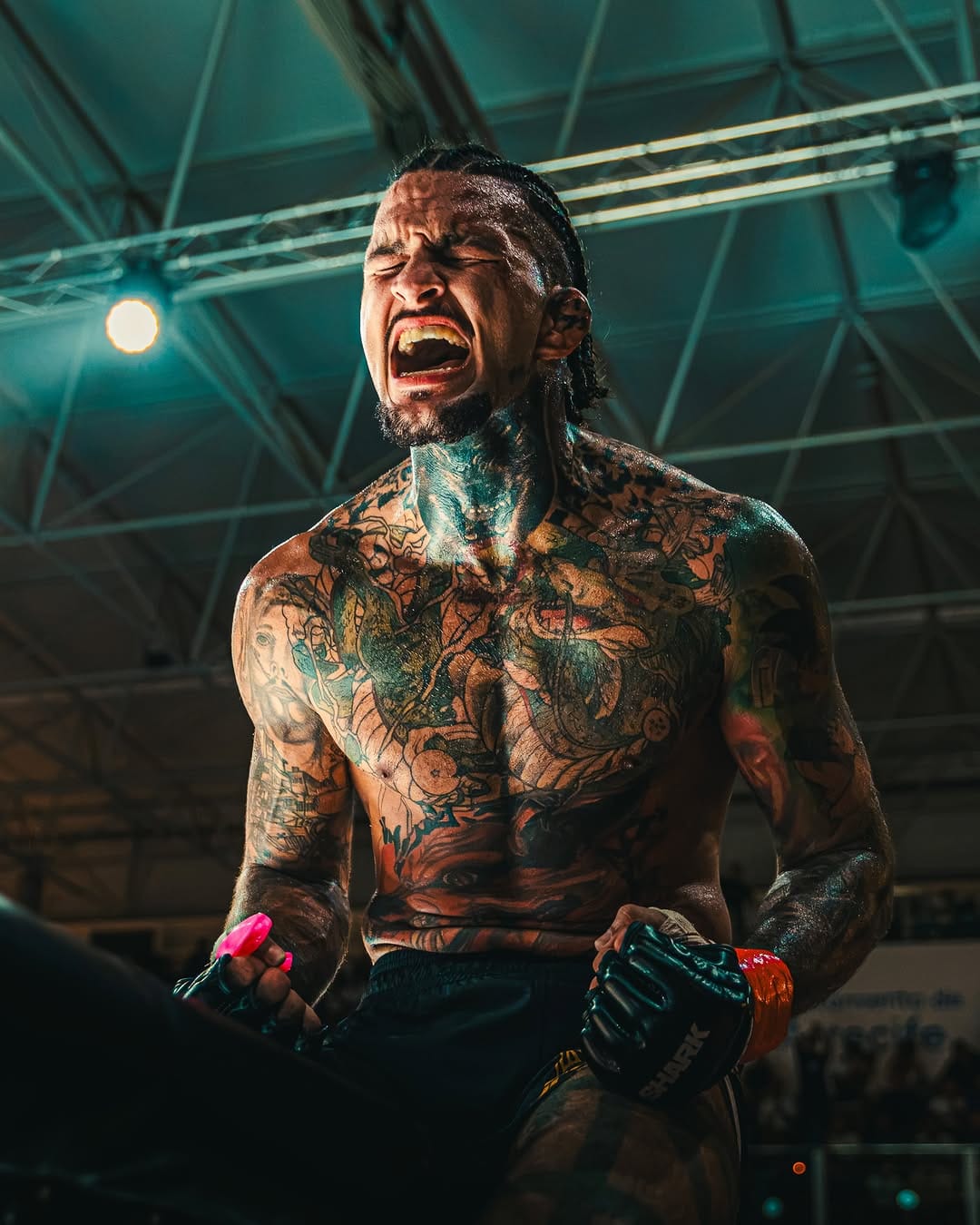 Sebas Santana grita de rodillas en la jaula, con el cuerpo tatuado y los guantes puestos