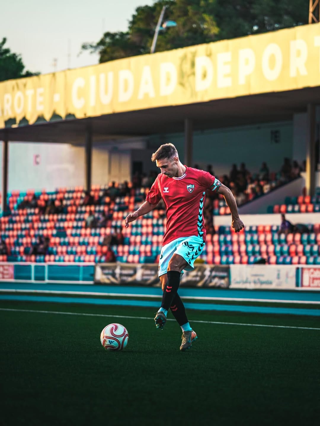 Jugador de rojo golpea el balón bajo el rótulo de la Ciudad Deportiva