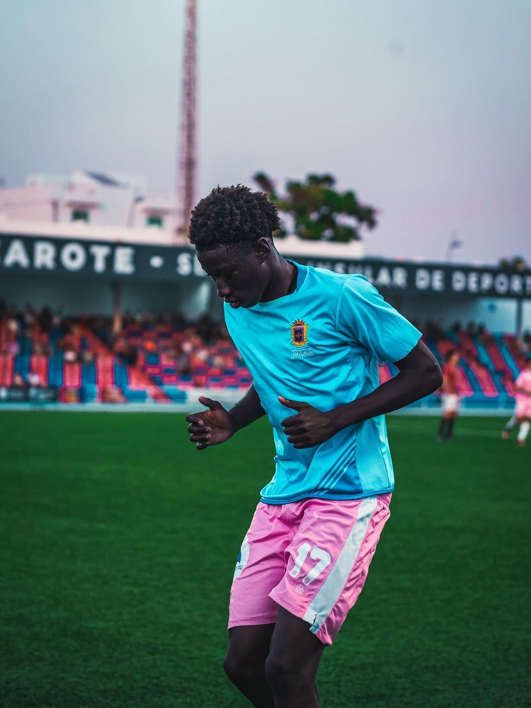 Jugador de rosa y azul controla el balón al atardecer